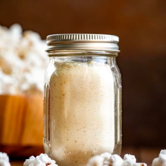 Jar of White Cheddar Popcorn Seasoning on a wooden table with popcorn in the background.