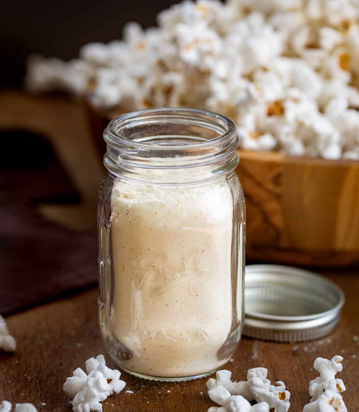 A quick and easy way to make your popcorn cheesy, flavorful, and irresistible. Just mix the spices and cheddar powder, shake on your favorite snack, and enjoy a homemade savory treat that’s ready in minutes! Jar of White Cheddar Popcorn Seasoning on a wooden table with popcorn in the background.