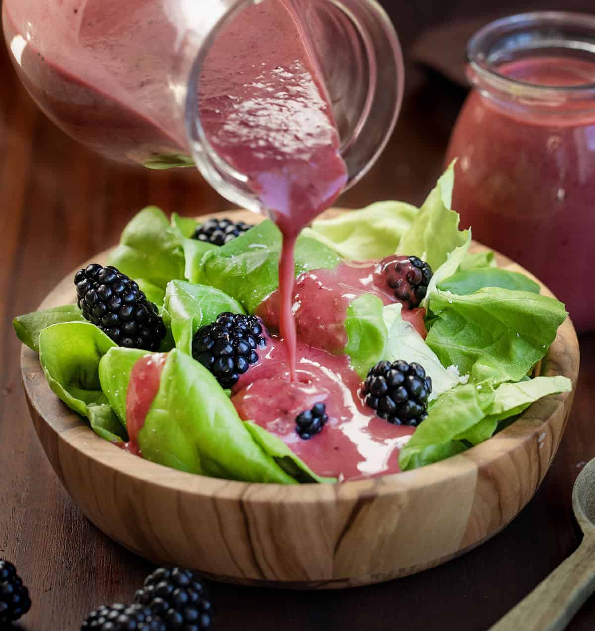 Pouring Blackberry Vinaigrette over a salad.