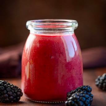 Bottle of Blackberry Vinaigrette on a wooden table with fresh blackberries.