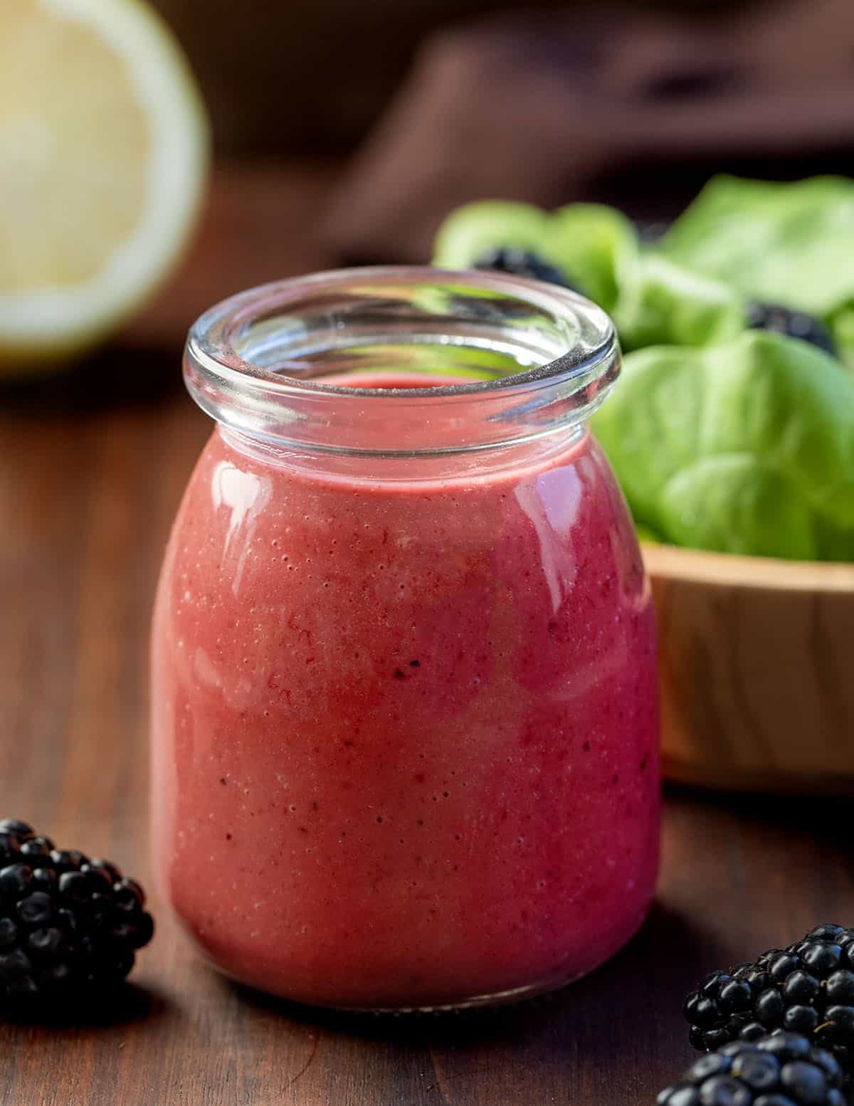 Bottle of Blackberry Vinaigrette on a table with fresh blackberries and a salad.