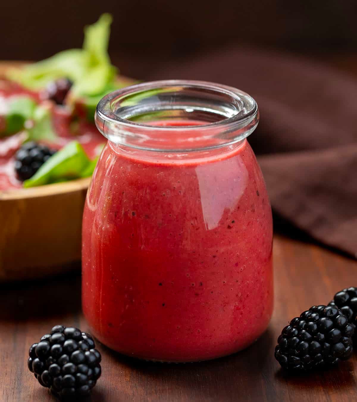 Bottle of Blackberry Vinaigrette on a wooden table with fresh blackberries and a salad.