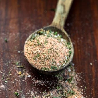 Wooden measuring spoon with Blackened Ranch Seasoning in it and some spilling on the wooden table.