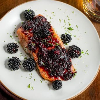 One plate of Bourbon Blackberry Salmon on a wooden table with a glass of bourbon.