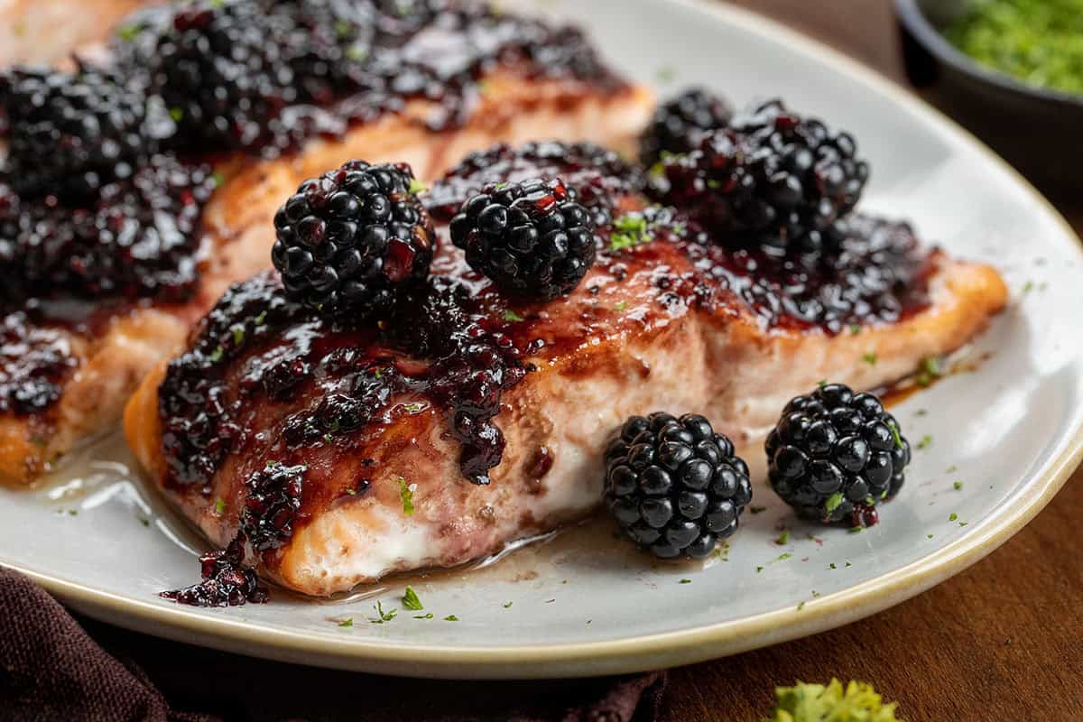 This bourbon blackberry salmon is a sweet and savory dinner made with tender baked salmon and a rich blackberry bourbon sauce. It’s bold, flavorful, and surprisingly easy to make for a restaurant-quality meal at home. Very close up on a piece of Bourbon Blackberry Salmon.