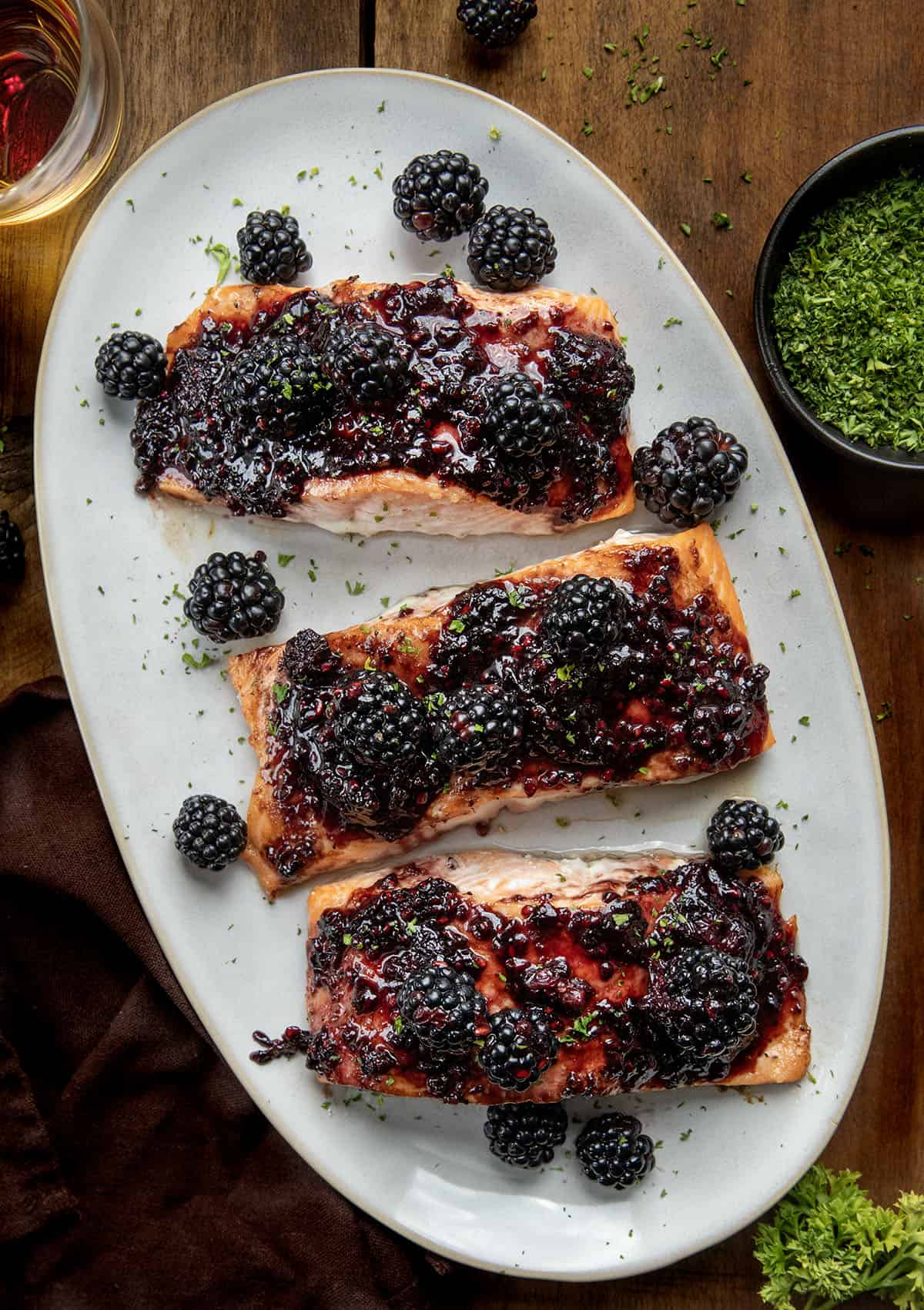 This bourbon blackberry salmon is a sweet and savory dinner made with tender baked salmon and a rich blackberry bourbon sauce. It’s bold, flavorful, and surprisingly easy to make for a restaurant-quality meal at home. Bourbon Blackberry Salmon on a platter on a wooden table from overhead.