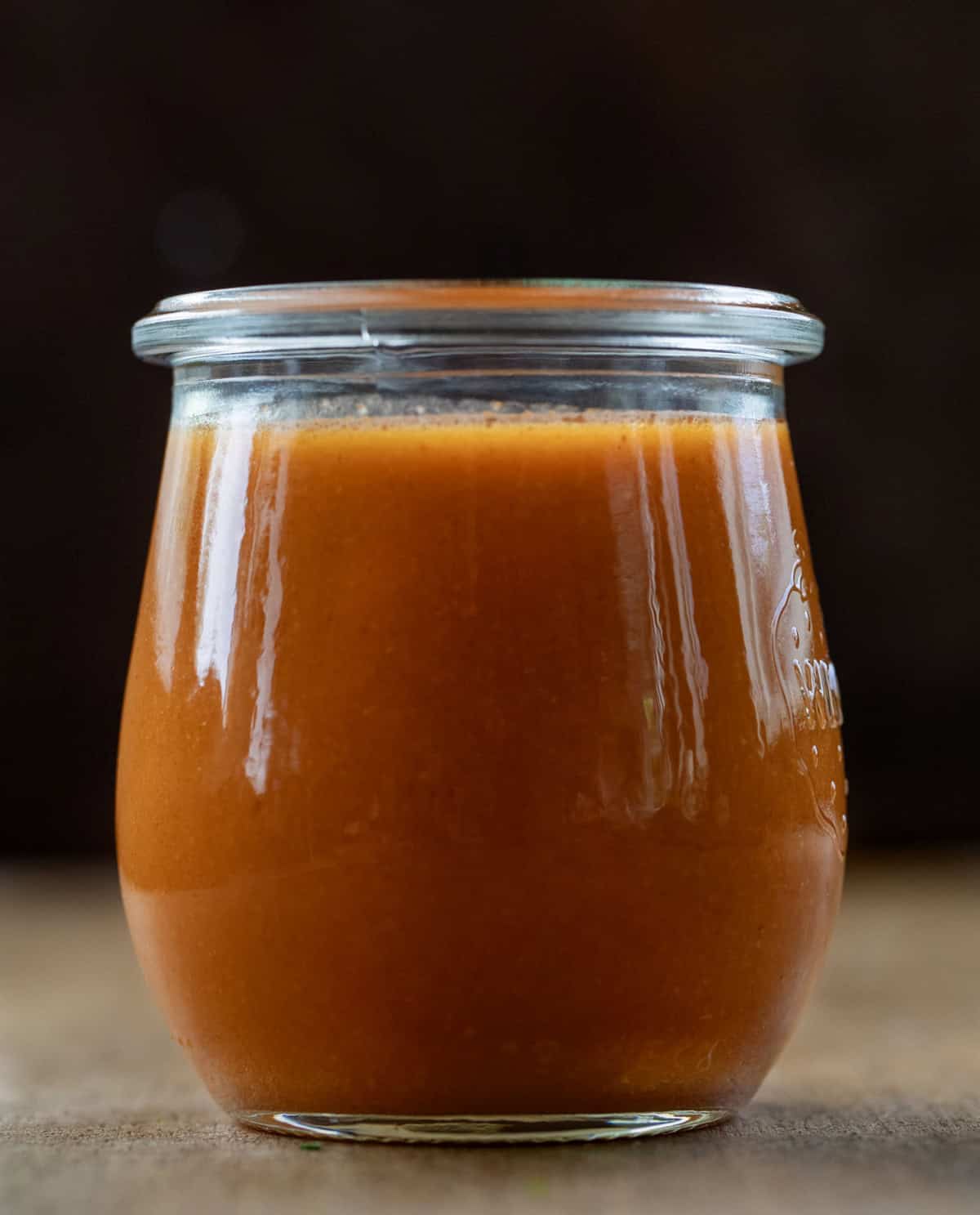 This Buffalo Sauce is rich, buttery, and packed with bold, tangy heat. It comes together in just minutes on the stovetop for a smooth, glossy sauce that clings perfectly to wings, chicken, and more. It’s quick, easy, and so much better than anything store-bought! Jar of Buffalo Sauce on a wooden table close up.