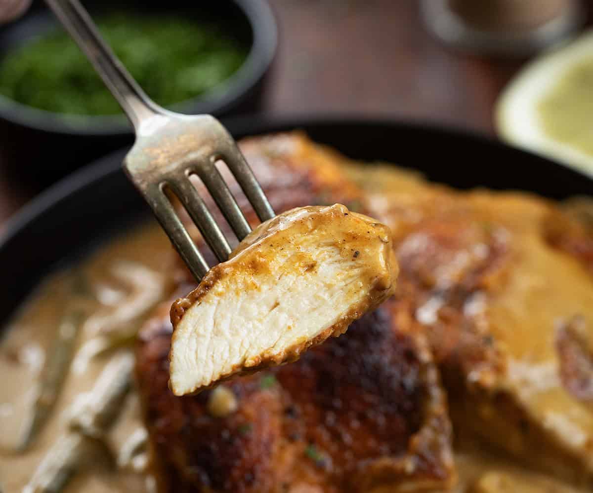 This Cajun Chicken and Gravy is an easy skillet dinner made with tender pan-seared chicken and a creamy onion and pepper gravy. Piece of chicken on a fork held above the Cajun Chicken and Gravy pan.