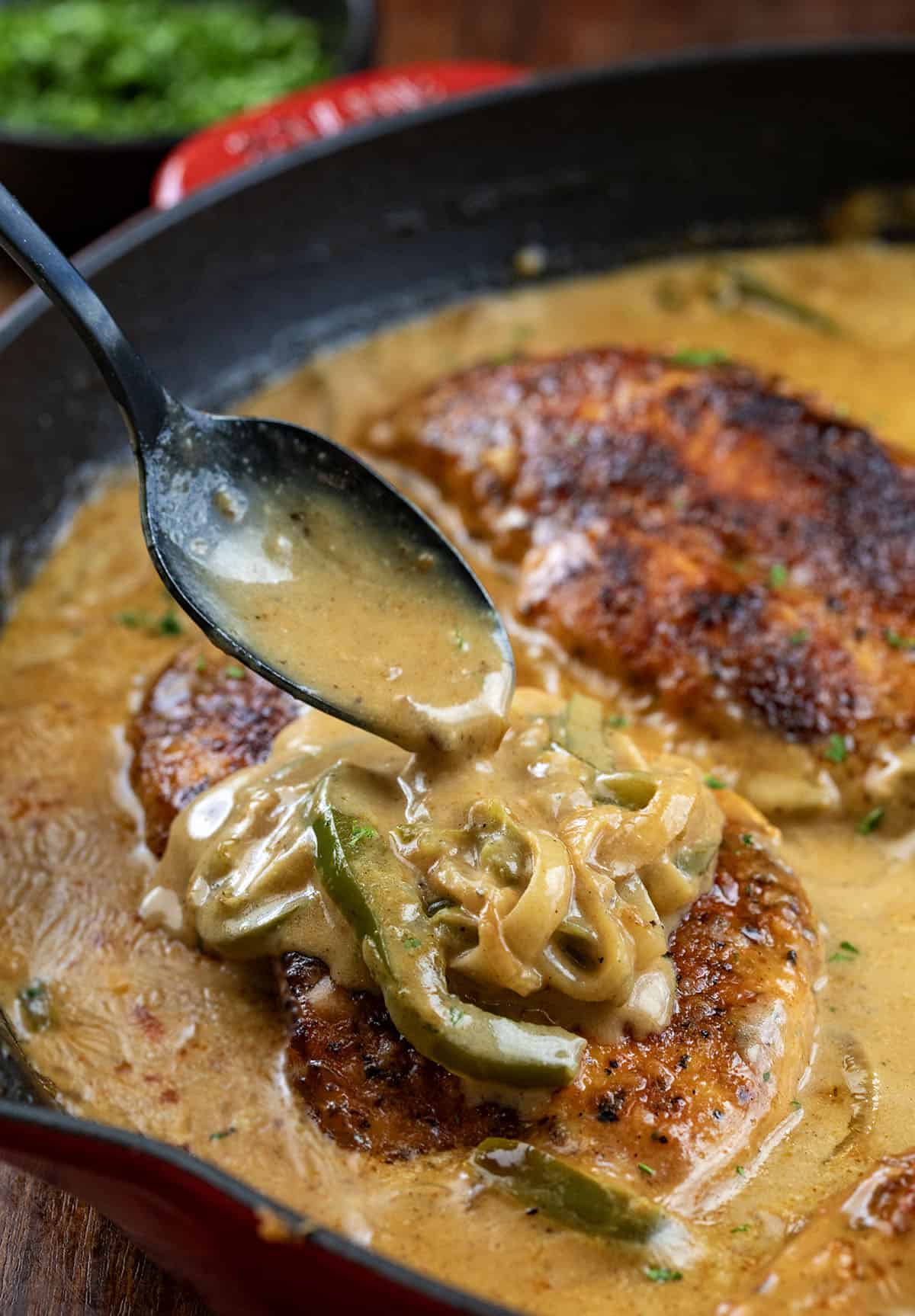 This Cajun Chicken and Gravy is an easy skillet dinner made with tender pan-seared chicken and a creamy onion and pepper gravy. Spooning pepper and onion cajun gravy over chicken in a pan.