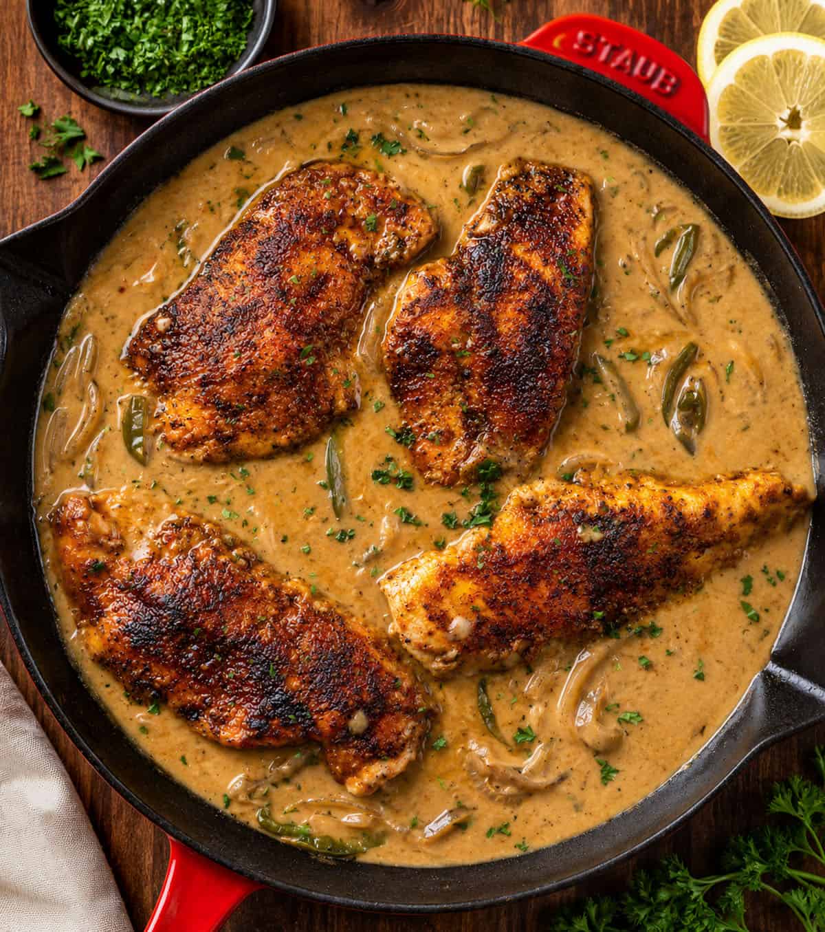 This Cajun Chicken and Gravy is an easy skillet dinner made with tender pan-seared chicken and a creamy onion and pepper gravy. Skillet of Cajun Chicken and Gravy on a wooden table from overhead.