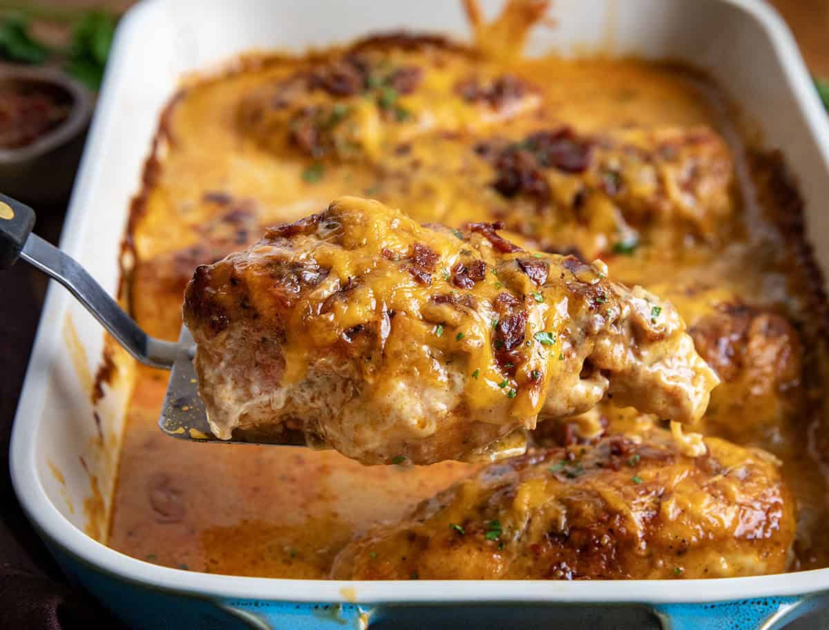 This Cheesy Ranch Chicken Casserole is a cozy baked dinner loaded with tender chicken, a creamy ranch cheese sauce, crispy bacon, and plenty of melted cheddar. It’s rich, comforting, and easy to throw together! Spatula holding a piece of Cheesy Ranch Chicken Casserole above the pan.