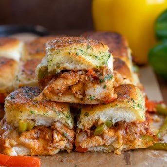 Chicken Fajita Sliders stacked on a wooden table with bell peppers in the background.