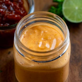 Jar of Chipotle Mayo with chipotle peppers and lime in the background.