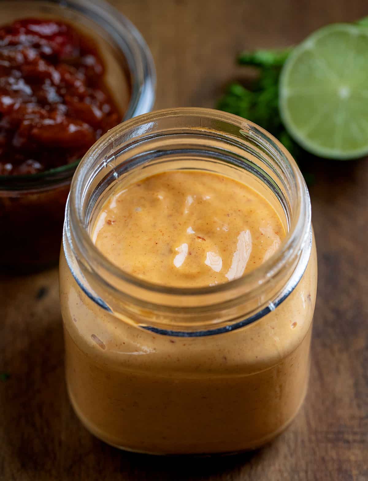 This Homemade Chipotle Mayo is creamy, smoky, and just the right amount of spicy with a touch of tangy lime and subtle sweetness. Jar of Chipotle Mayo with chipotle peppers and lime in the background.