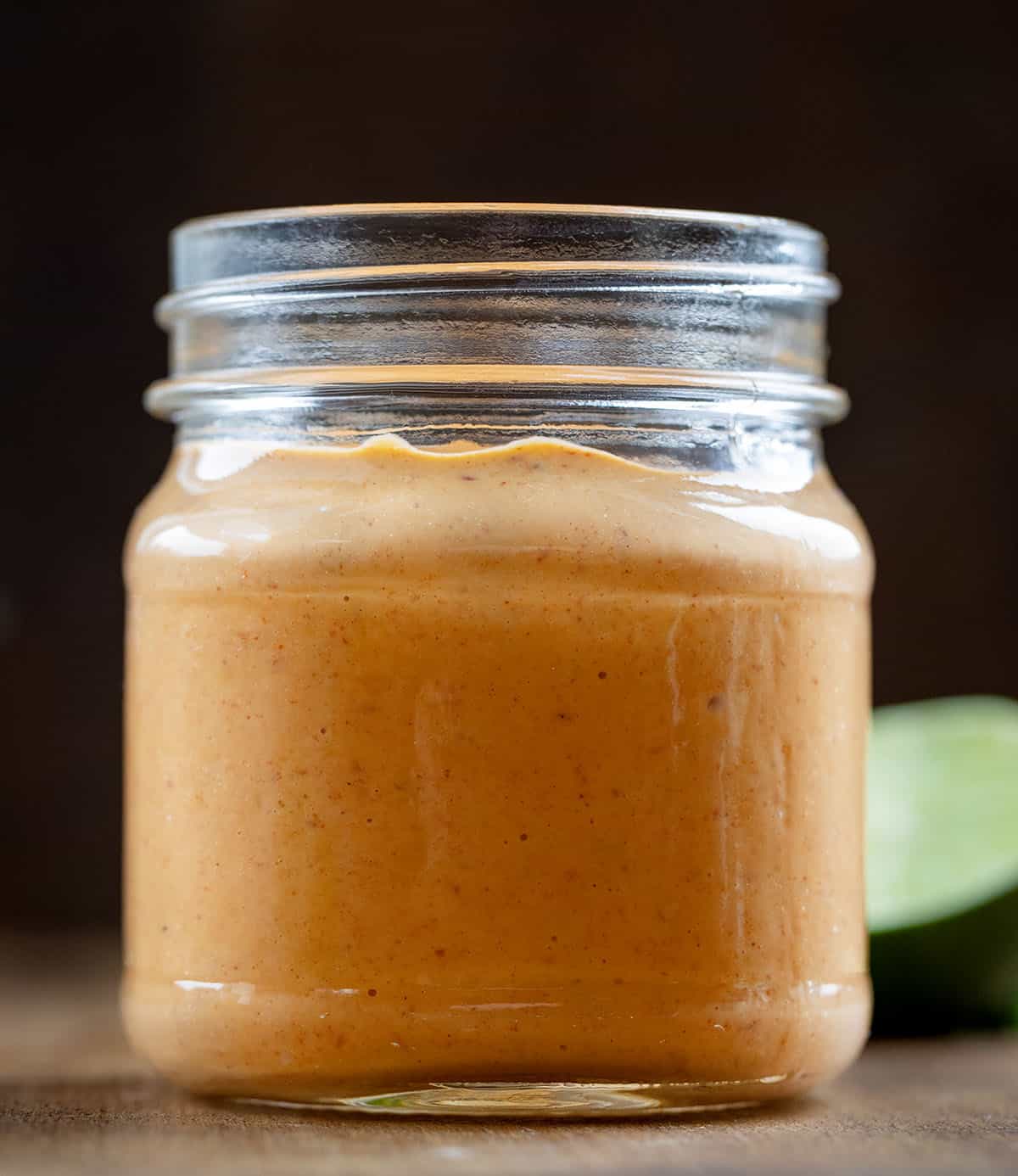 This Homemade Chipotle Mayo is creamy, smoky, and just the right amount of spicy with a touch of tangy lime and subtle sweetness. Jar of Chipotle Mayo on a wooden table with fresh cut lime in the back.