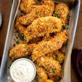 Pan of Cornflake Chicken with some ranch dressing on a wooden table.