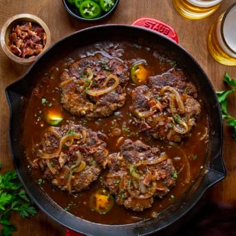 Skillet of Cowboy Salisbury Steak on a wooden table with jalapeno and beer.