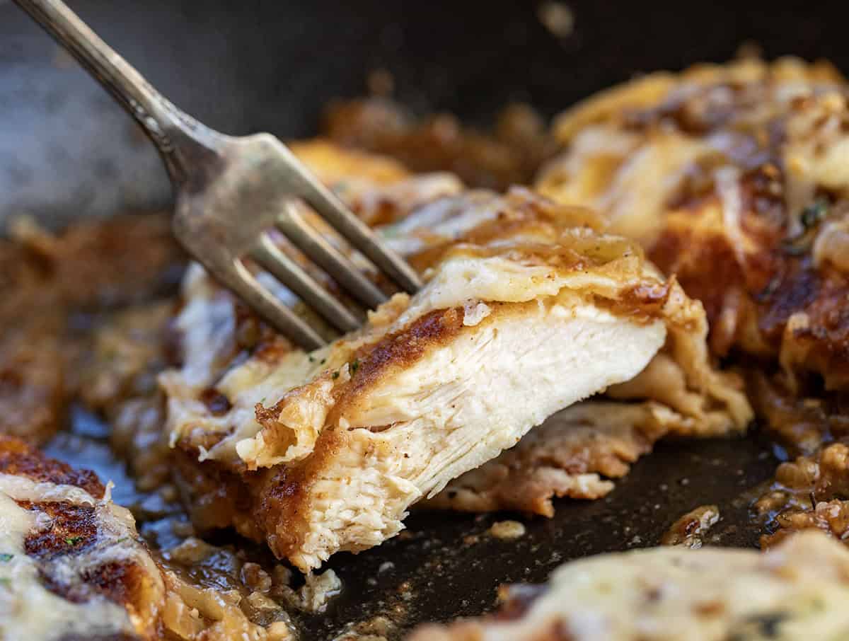 This French Onion Breaded Chicken is a cozy skillet dinner made with crispy breaded chicken, sweet caramelized onions, and melted Gruyère cheese. It’s rich, savory, and full of classic French onion flavor! Cut into piece of French Onion Breaded Chicken being held up by a fork.