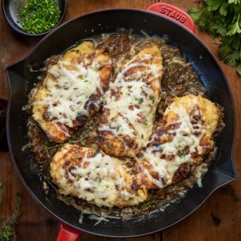 Skillet of French Onion Breaded Chicken on a wooden table from overhead.