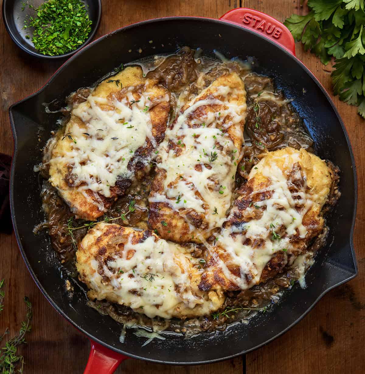 This French Onion Breaded Chicken is a cozy skillet dinner made with crispy breaded chicken, sweet caramelized onions, and melted Gruyère cheese. It’s rich, savory, and full of classic French onion flavor! Skillet of French Onion Breaded Chicken on a wooden table from overhead.
