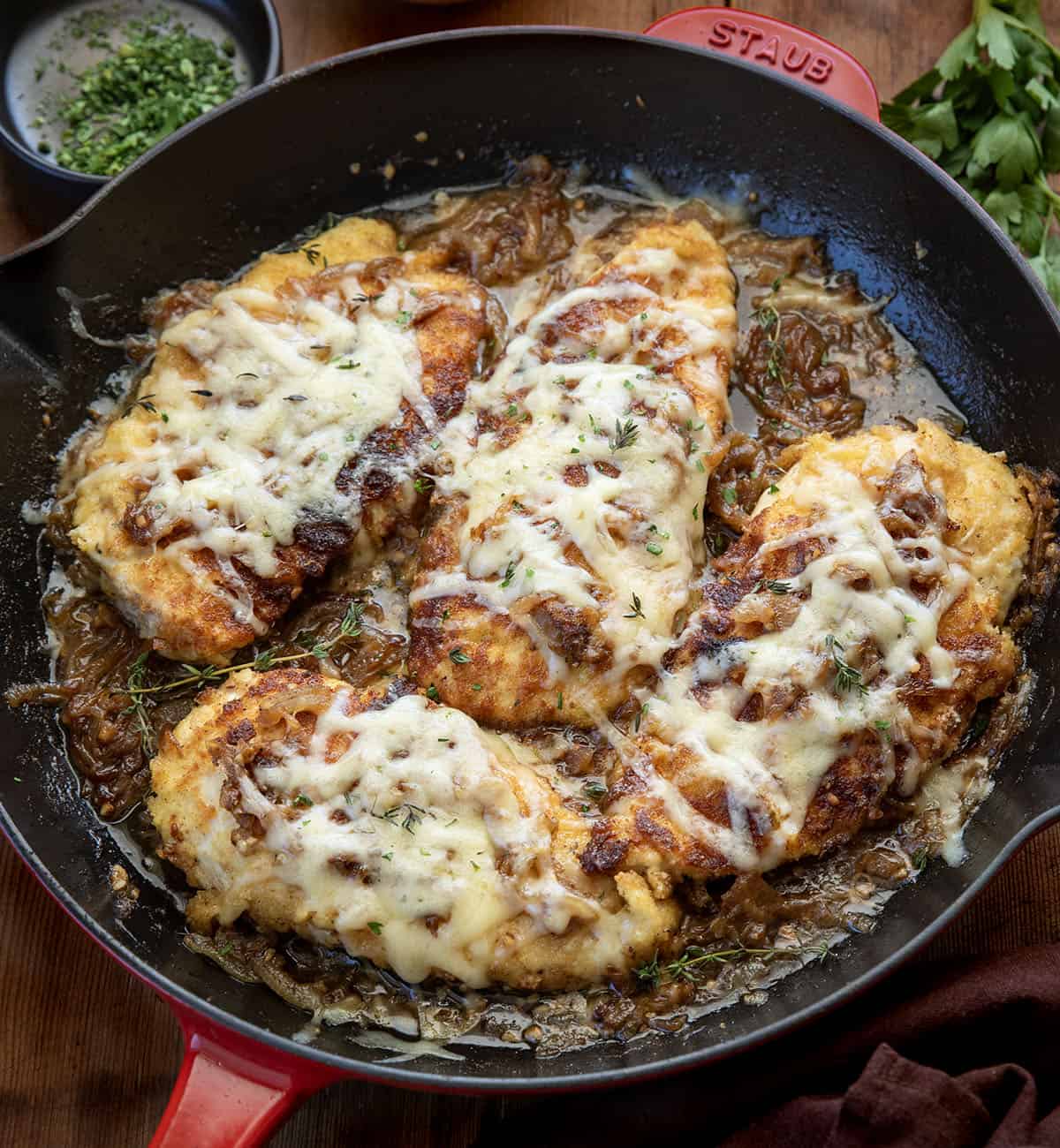 This French Onion Breaded Chicken is a cozy skillet dinner made with crispy breaded chicken, sweet caramelized onions, and melted Gruyère cheese. It’s rich, savory, and full of classic French onion flavor! Skillet of French Onion Breaded Chicken on a wooden table from overhead.