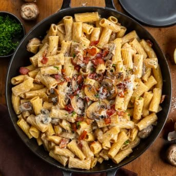 Skillet of Mushroom and Bacon Rigatoni on a wooden table from overhead.
