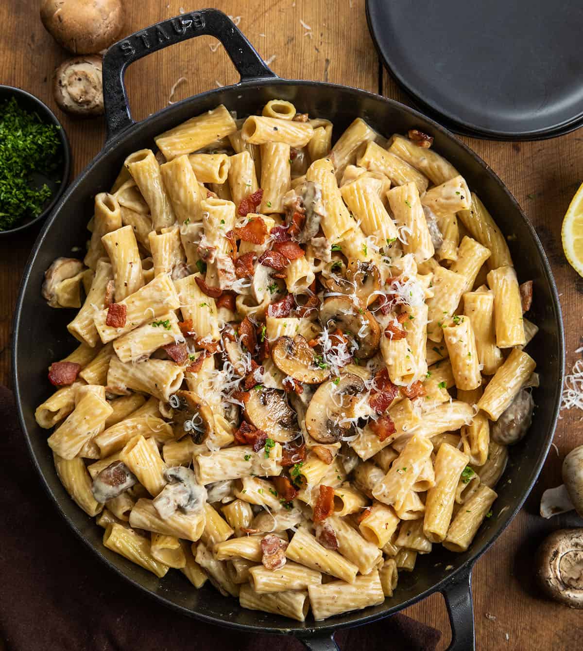 This mushroom and bacon rigatoni is a rich, creamy pasta made with crispy bacon, sautéed mushrooms, and a silky Parmesan cream sauce. It’s hearty, comforting, and full of deep savory flavor, with a touch of lemon to keep it balanced. Skillet of Mushroom and Bacon Rigatoni on a wooden table from overhead.