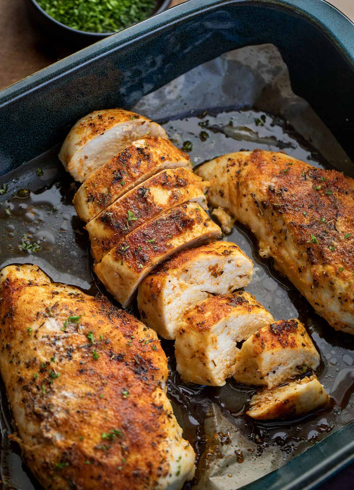 Oven Baked Chicken Breasts in a pan with one sliced.