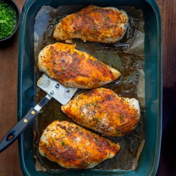 Oven Baked Chicken Breasts with a spatula in the pan on a wooden table from overhead.