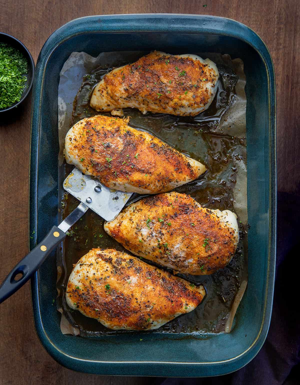Oven Baked Chicken Breasts with a spatula in the pan on a wooden table from overhead.
