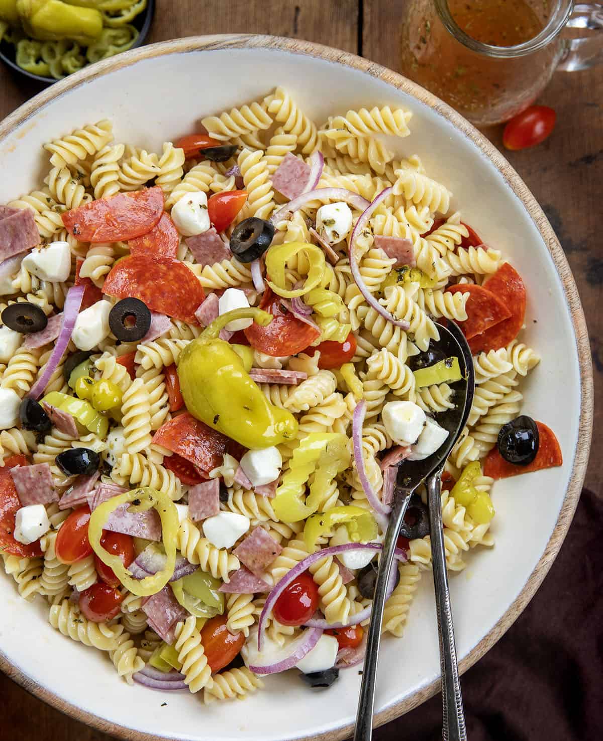 This Pepperoncini Pasta Salad is bold, tangy, and packed with all the good stuff. Tender rotini is tossed with mozzarella, pepperoni, salami, fresh veggies, and plenty of pepperoncini for that zesty bite in every forkful! Large bowl of Pepperoncini Pasta Salad with salad tongs in it from overhead.