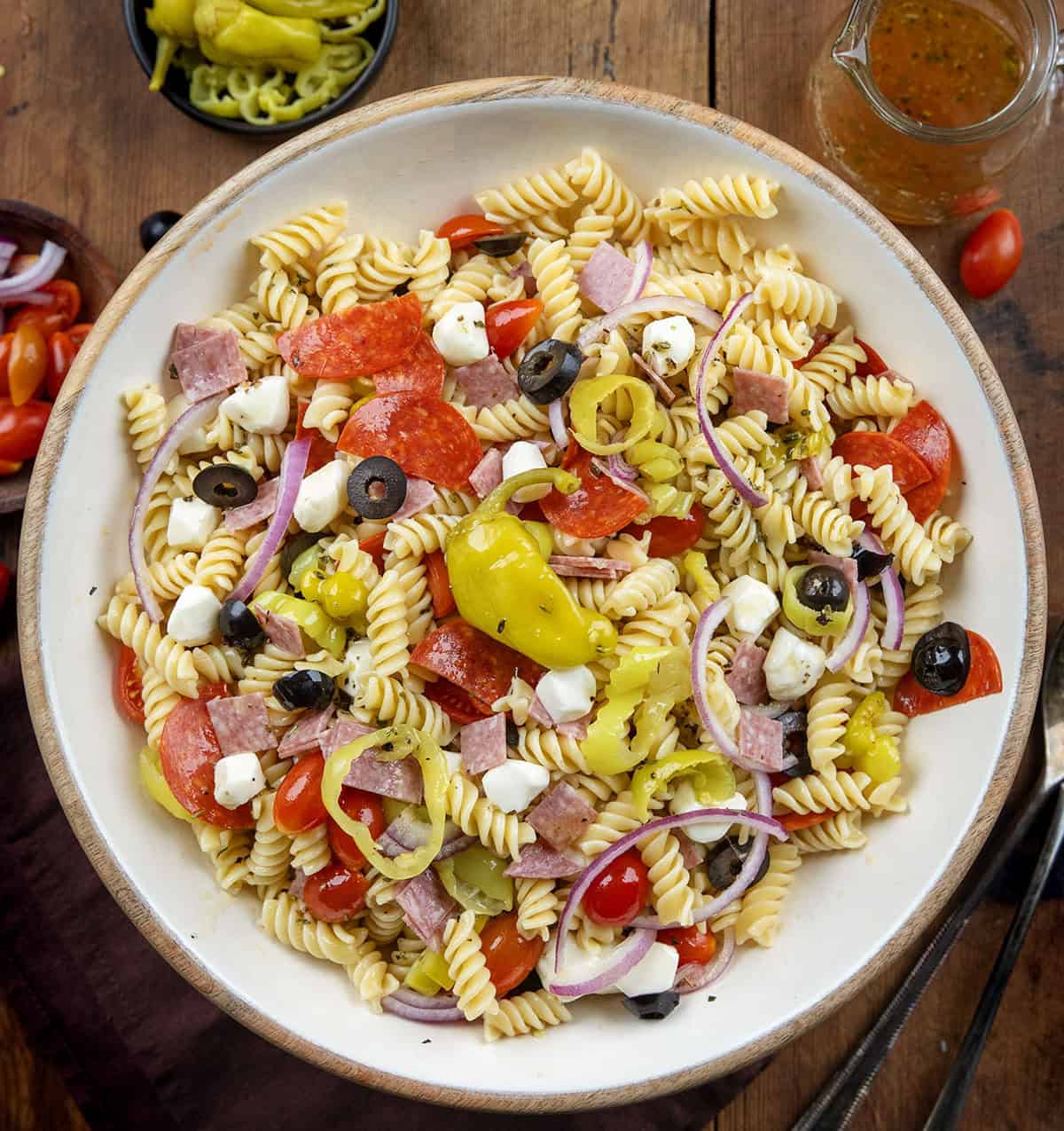 This Pepperoncini Pasta Salad is bold, tangy, and packed with all the good stuff. Tender rotini is tossed with mozzarella, pepperoni, salami, fresh veggies, and plenty of pepperoncini for that zesty bite in every forkful! Large bowl of Pepperoncini Pasta Salad on a wooden table from overhead.