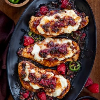 Black platter of Raspberry Jalapeño Cream Cheese Chicken on a wooden table from overhead.