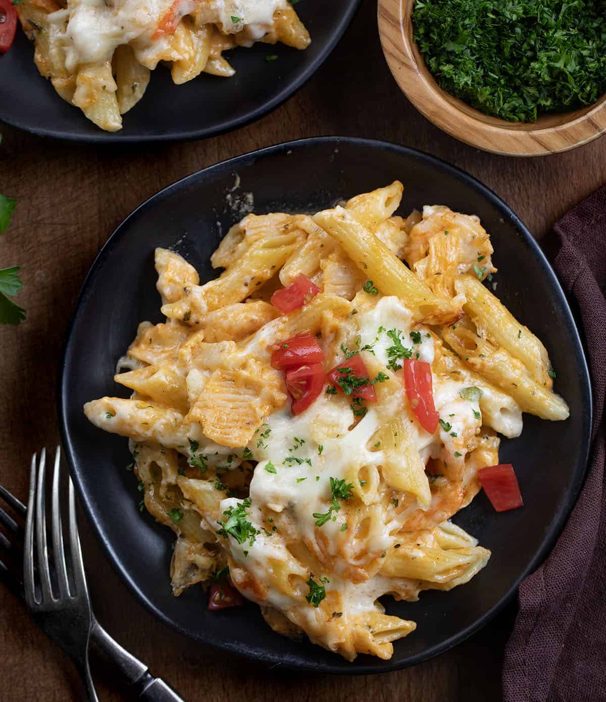 This Creamy Seafood Pasta Bake is a rich, comforting baked pasta loaded with tender shrimp, imitation crab, and a creamy Monterey Jack cheese sauce. It’s baked until bubbly and golden on top, making it an easy yet impressive dinner that’s perfect for seafood lovers! Black plates with Seafood Pasta Bake on them on a wooden table from overhead.