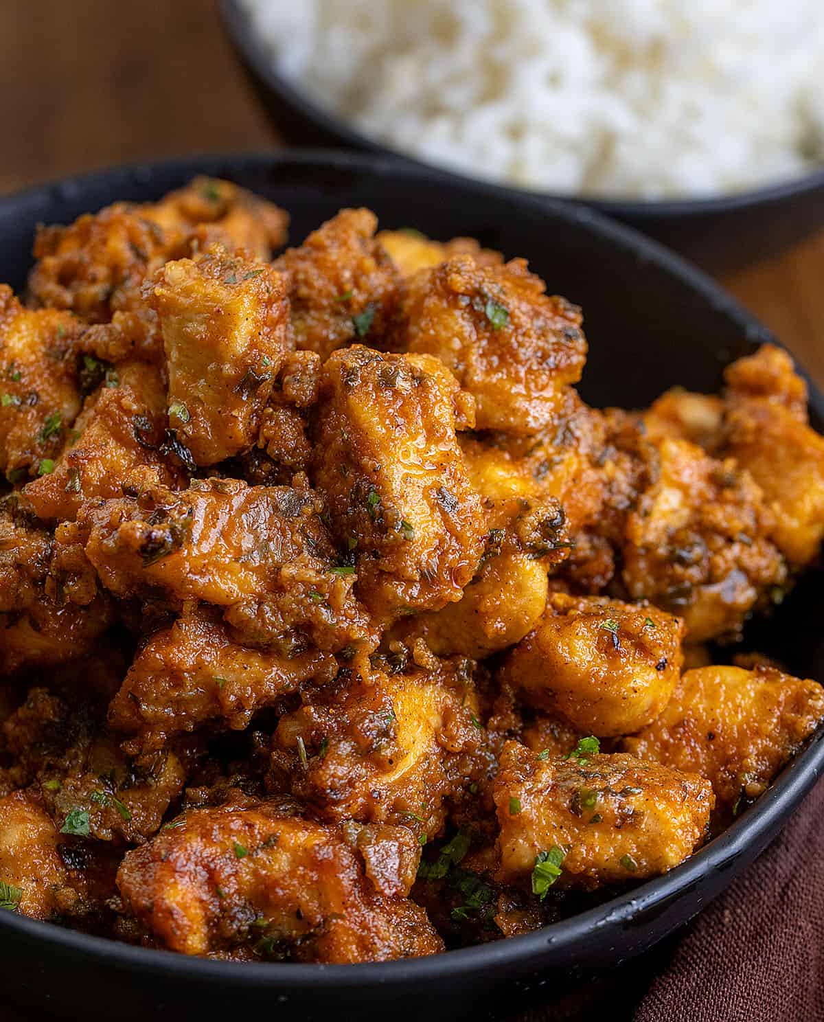 This Sheet Pan Buffalo Chicken is one of those easy, high-flavor dinners that hits all the right notes! You get tender, juicy chicken, and plenty of bold buffalo flavor in every bite! Black plate with Sheet Pan Buffalo Chicken in it next to a bowl of rice.