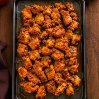 Black sheet pan with Buffalo Chicken Bites on it on a wooden table from overhead.