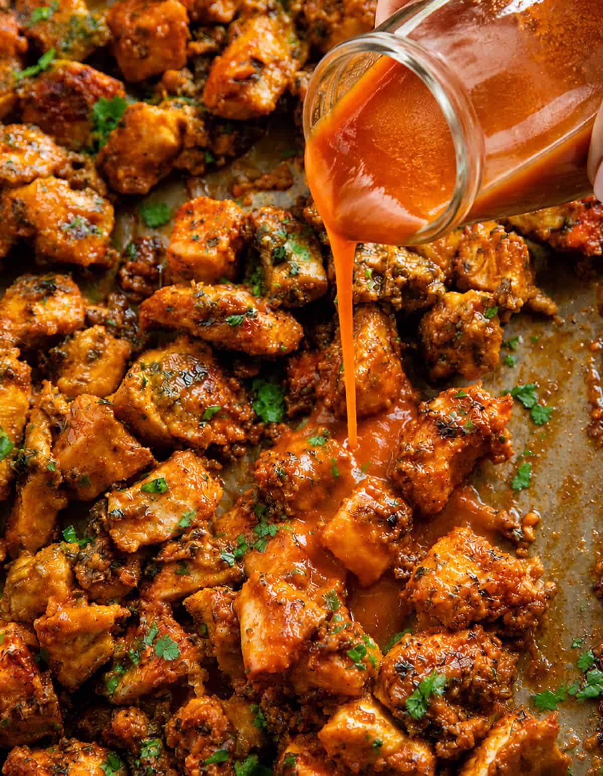 This Sheet Pan Buffalo Chicken is one of those easy, high-flavor dinners that hits all the right notes! You get tender, juicy chicken, and plenty of bold buffalo flavor in every bite! Pouring Buffalo Sauce over Sheet Pan Buffalo Chicken.