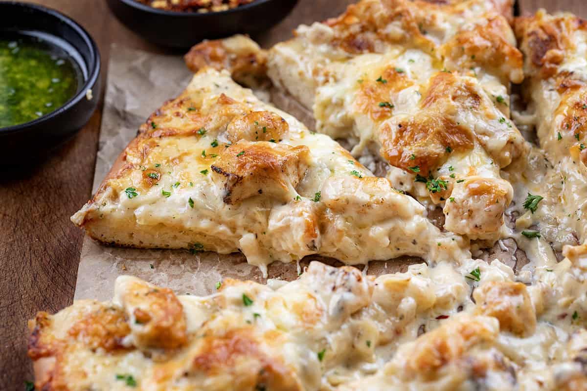 Close up of a piece of Chicken Alfredo Pizza with sauce dripping down sides.