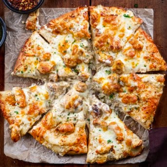 Chicken Alfredo Pizza on a wooden table that has been cut into 8 pieces.