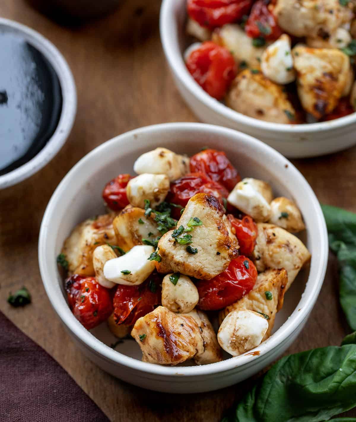 Bowls of Chicken Caprese Skewers off of the skewer on a wooden table Bowls of Chicken Caprese Skewers off of the skewer on a wooden table.