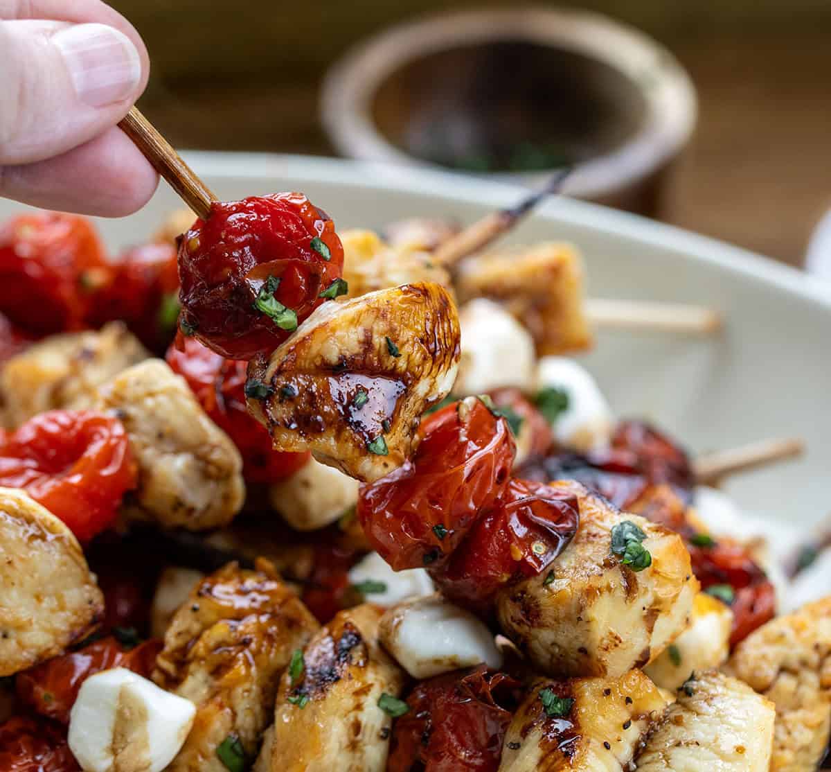 Hand holding a Chicken Caprese Skewer above the platter Hand holding a Chicken Caprese Skewer above the platter.