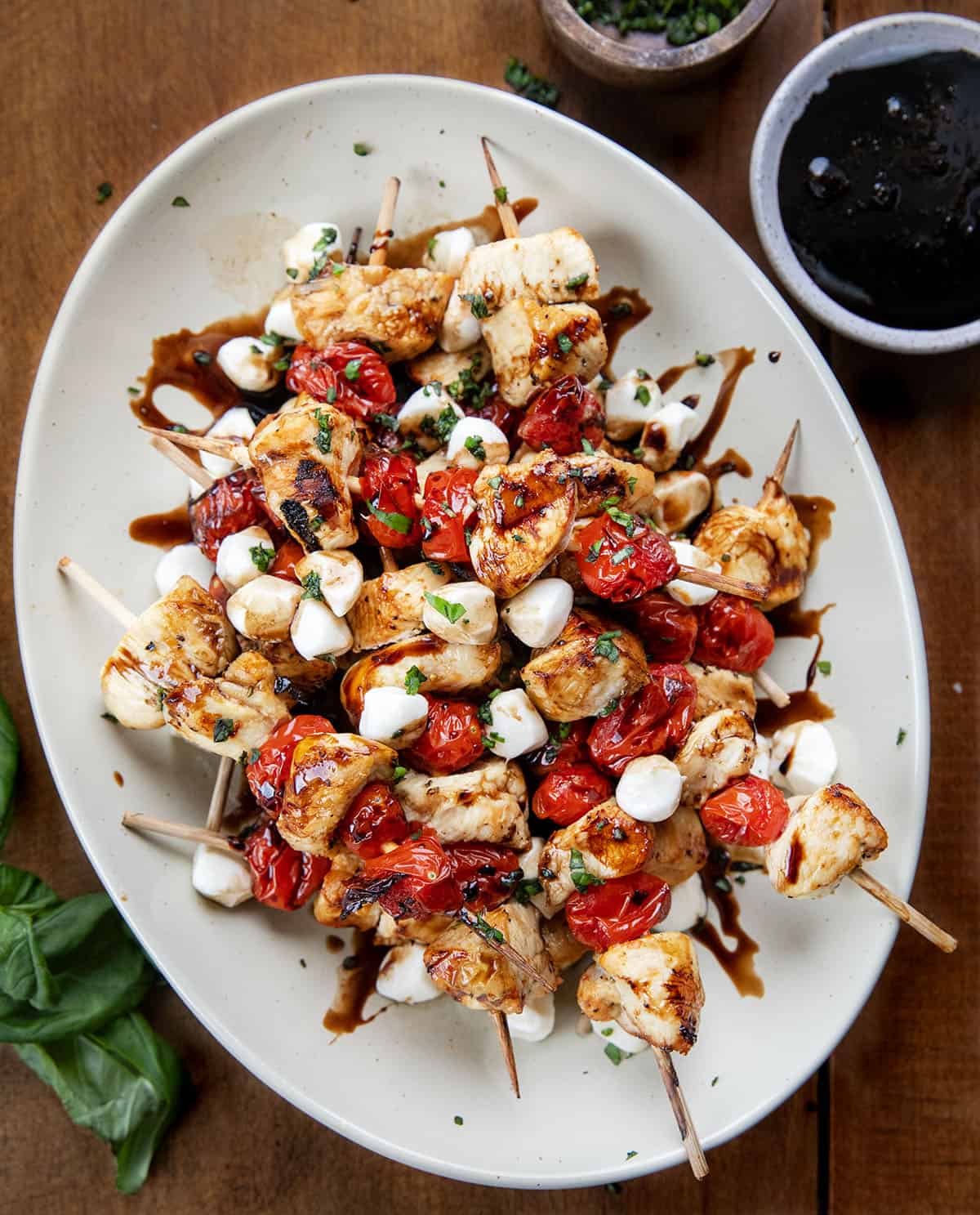 Chicken Caprese Skewers on a platter on a wooden table with basil and balsamic sauce Chicken Caprese Skewers on a platter on a wooden table with basil and balsamic sauce.