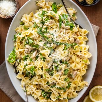 Serving platter of Chicken Lemon Parmesan Pasta Salad with serving spoons on a wooden table from overhead.