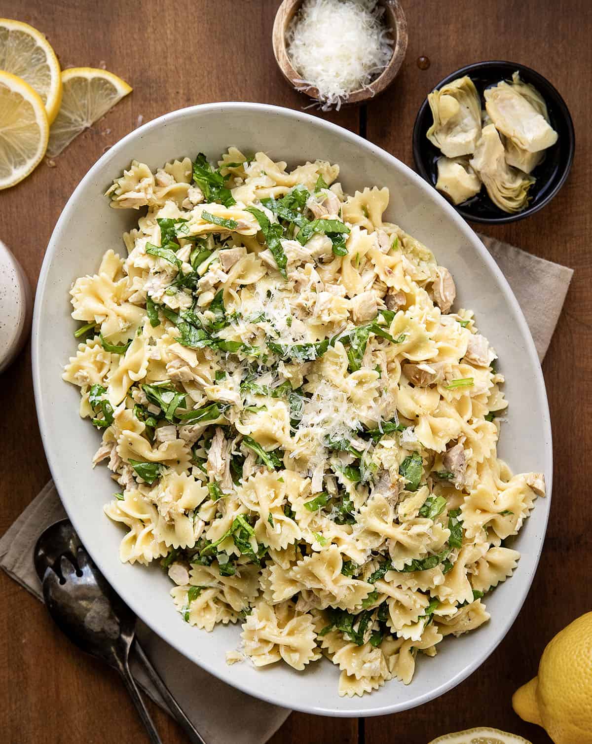 This Lemon Parmesan Pasta Salad with Chicken is a light, fresh pasta salad made with tender chicken, pasta, parmesan, and a bright lemon-garlic vinaigrette! Serving platter of Chicken Lemon Parmesan Pasta Salad on a wooden table from overhead.