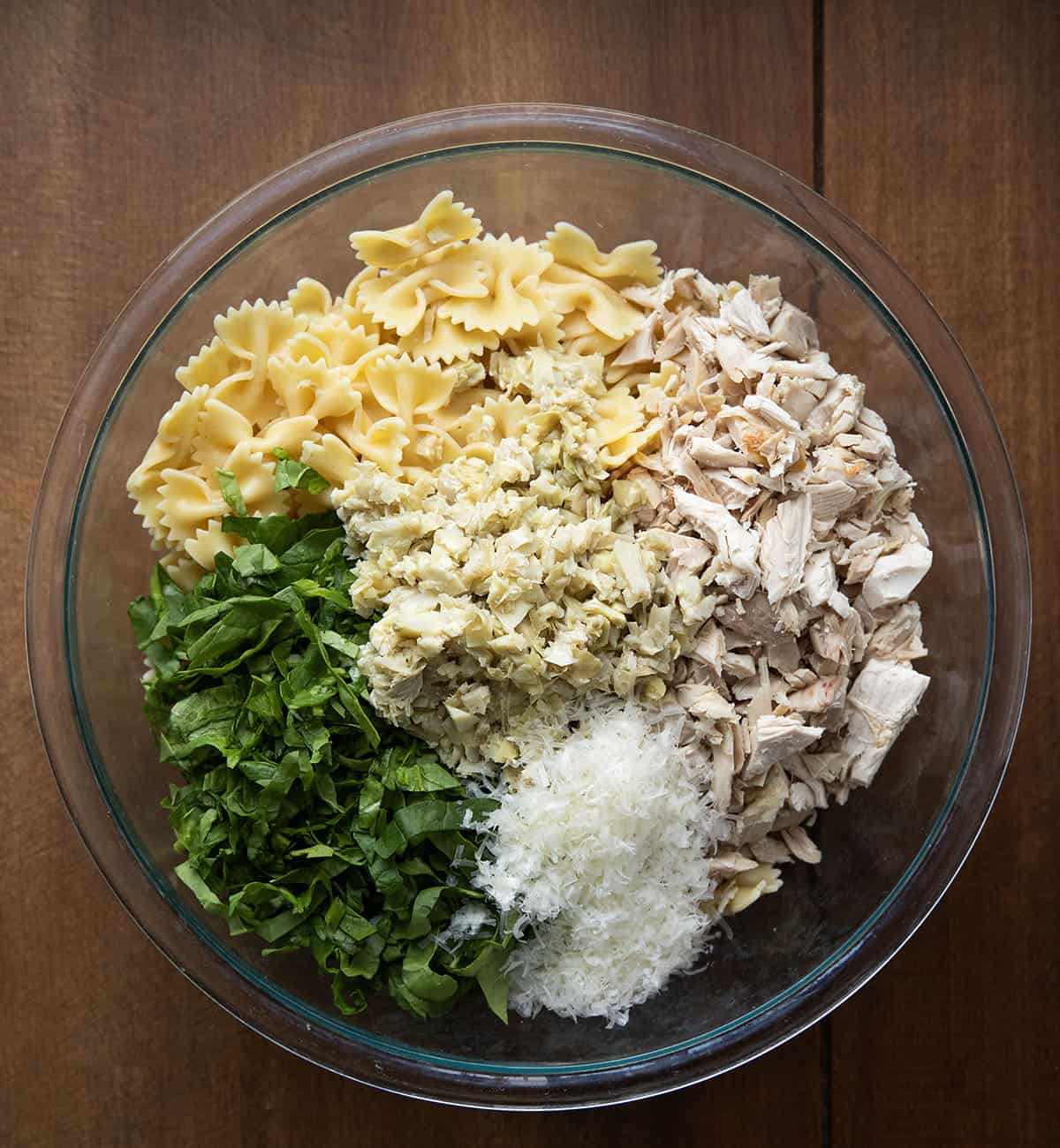 This Lemon Parmesan Pasta Salad with Chicken is a light, fresh pasta salad made with tender chicken, pasta, parmesan, and a bright lemon-garlic vinaigrette! Raw ingredients for Chicken Lemon Parmesan Pasta Salad in a bowl from overhead.