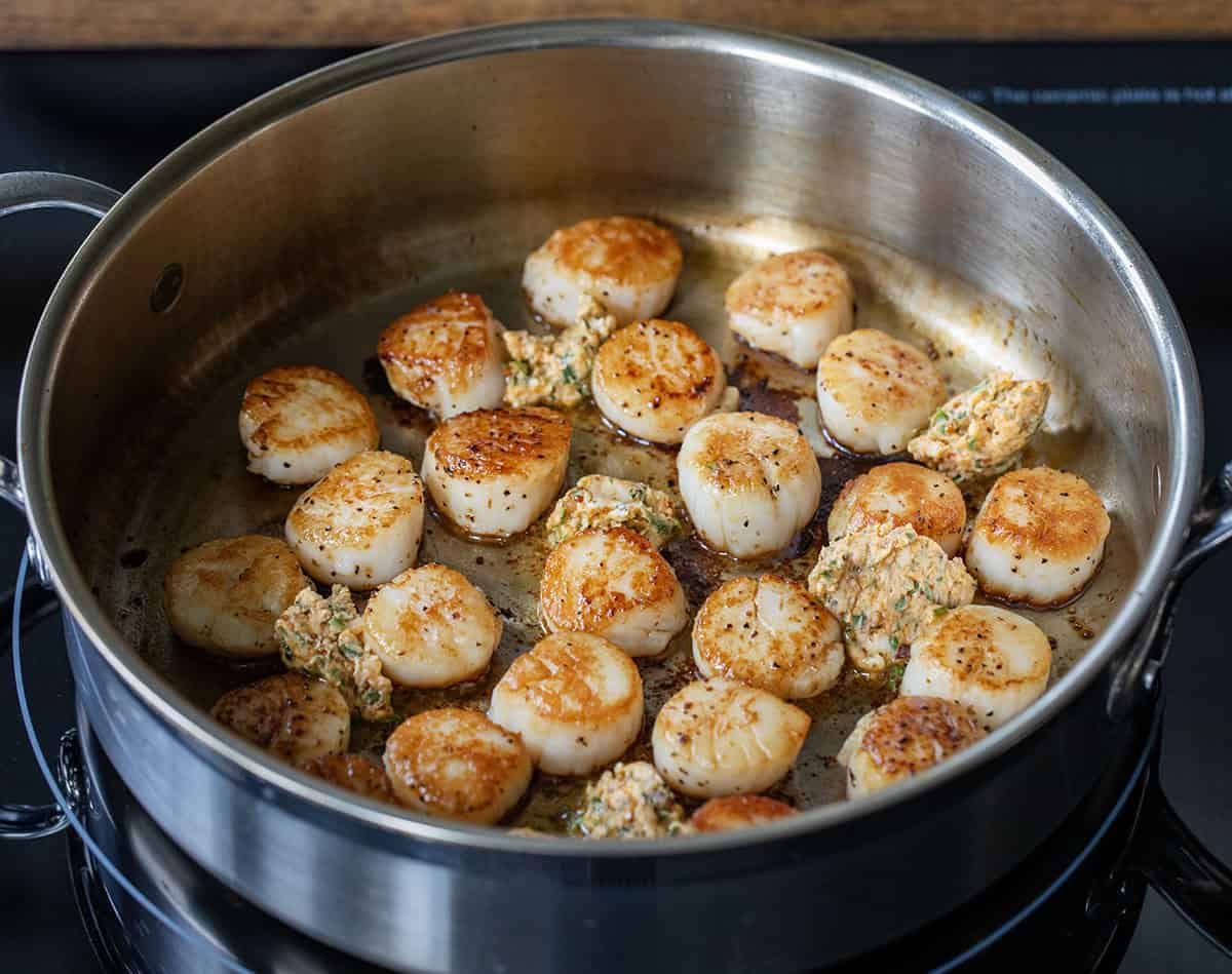 Cowboy butter added to a skillet with seared scallops Adding cowboy butter to the skillet of seared scallops.