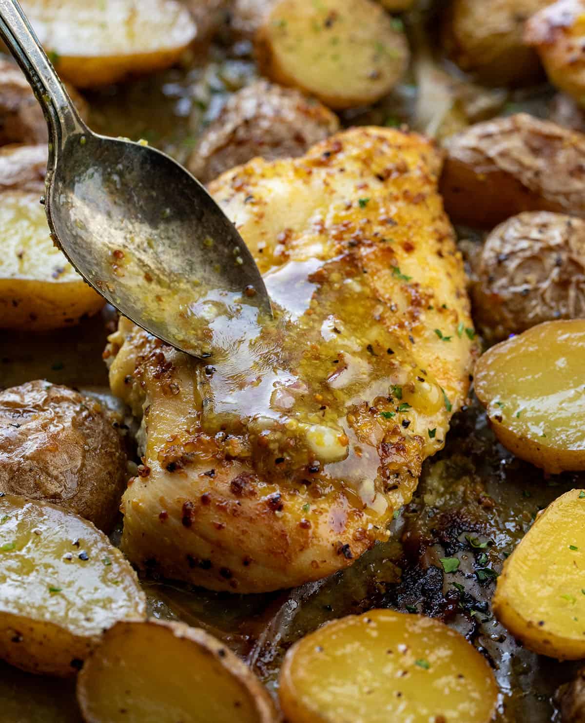 This One Pan Honey Mustard Chicken and Potatoes is an easy sheet pan dinner made with juicy marinated chicken, crispy roasted potatoes, and a sweet-tangy honey mustard glaze! Drizzling sauce over Honey Mustard Chicken and Potatoes.