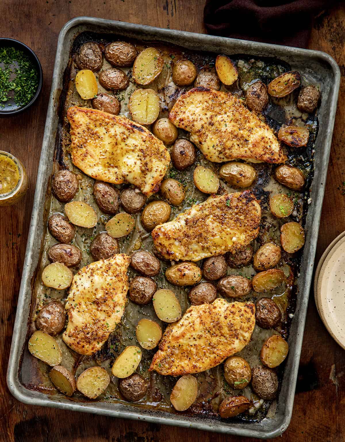 This One Pan Honey Mustard Chicken and Potatoes is an easy sheet pan dinner made with juicy marinated chicken, crispy roasted potatoes, and a sweet-tangy honey mustard glaze! Honey Mustard Chicken and POtatoes on a sheet pan on a wooden table from overhead.