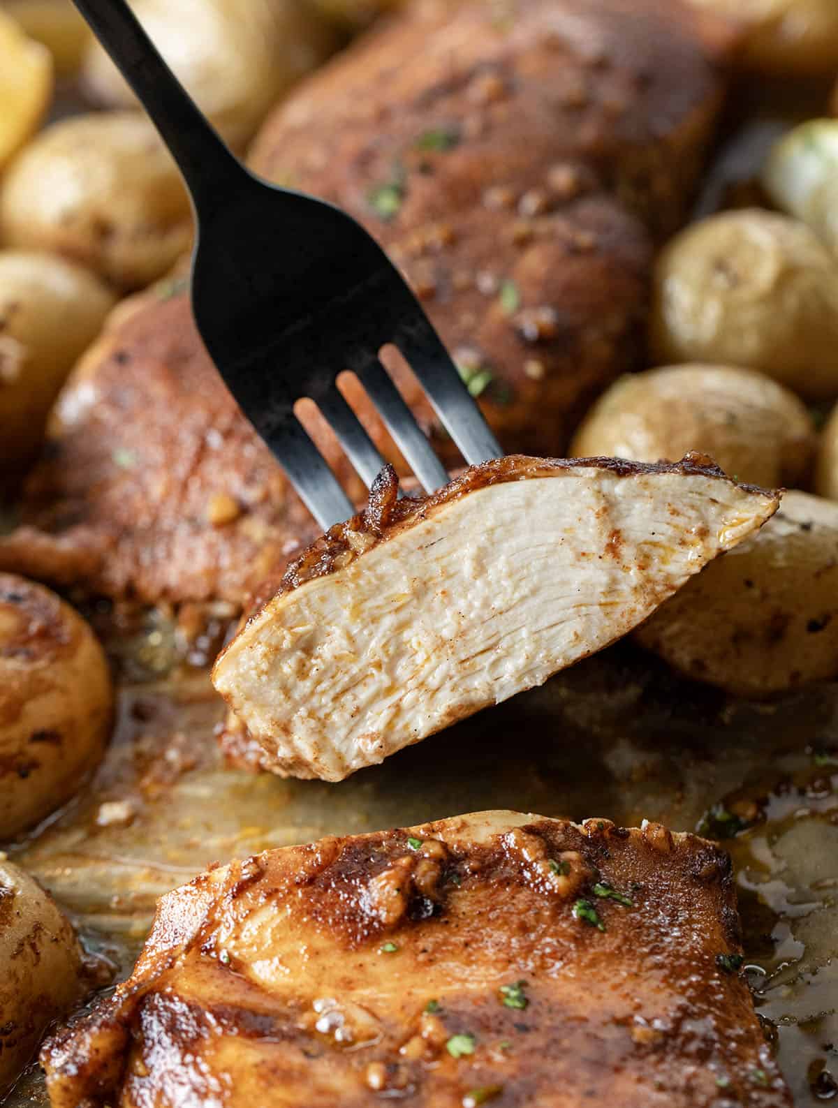 Juicy chicken and golden potatoes to a simple balsamic-lemon glaze that coats everything as it bakes Fork holding up a jicu piece of balsamic chicken.