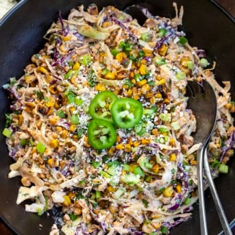 Close up of a bowl of Mexican Street Corn Slaw with serving spoons in it.